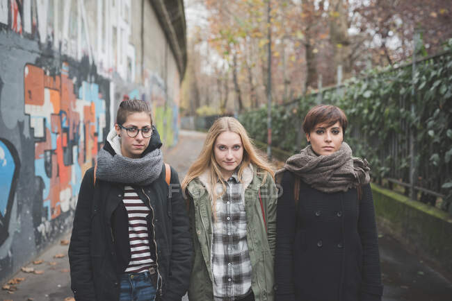 Три сестры проходят мимо стены с граффити — стоковое фото