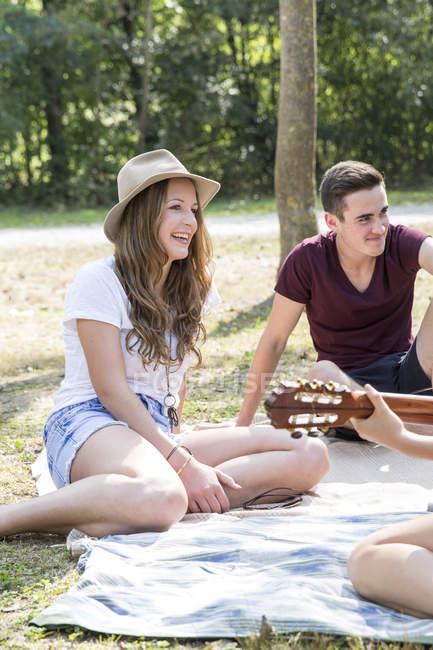 Gruppe junger Erwachsener sitzt auf Picknickdecke, junge Frau spielt Gitarre — Stockfoto