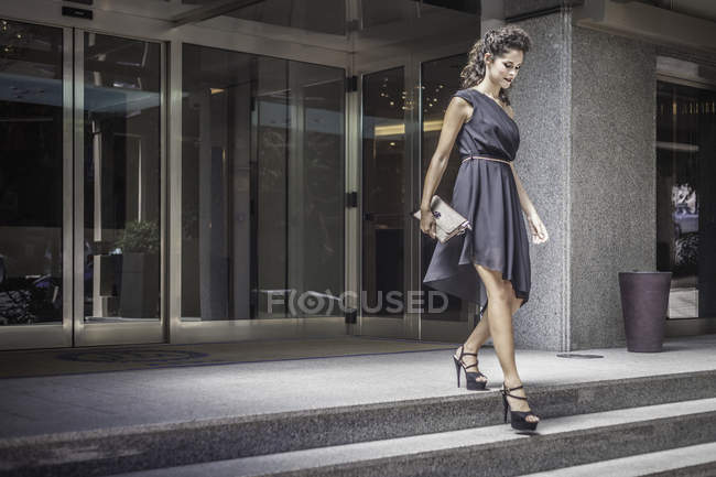Jovem mulher vestindo vestido preto descendo degraus — Fotografia de Stock