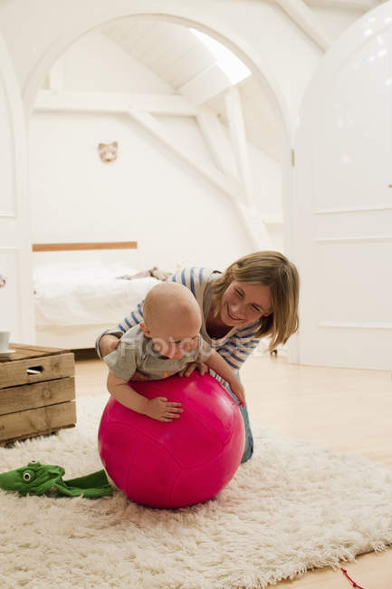 Madura madre y bebé hija en la parte superior de la bola de ejercicio en la sala de estar - foto de stock