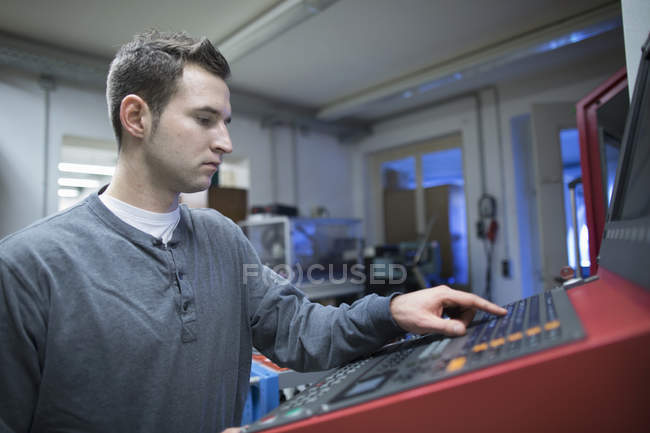 Jeune technicien masculin utilisant le panneau de commande pour la machine en atelier — Photo de stock