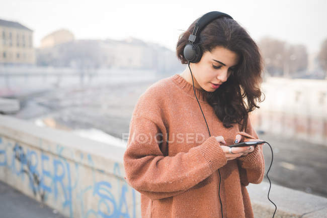 Молода жінка в навушниках вибирає музику на смартфон — стокове фото