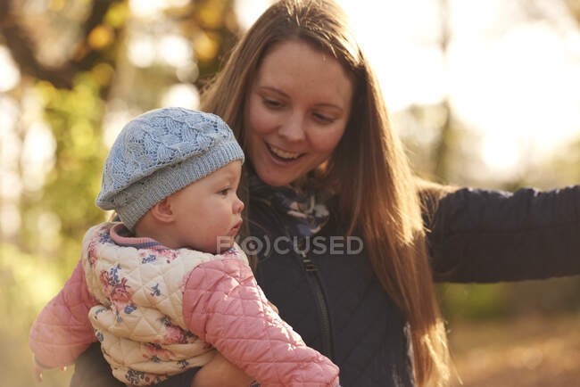 Mujer adulta e hija pequeña mirando hacia otro lado en el parque de otoño - foto de stock