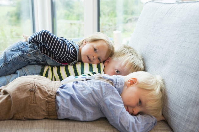Portrait of tired boy and two toddlers lying on sofa — Stock Photo