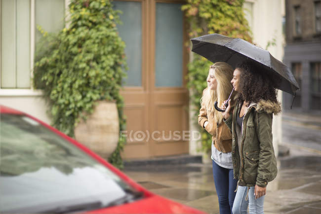 Mujeres jóvenes usando paraguas en la calle de la ciudad - foto de stock