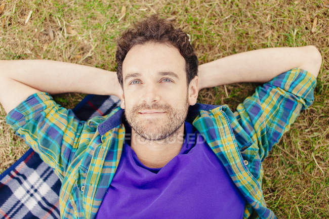 Visão de ângulo alto do homem adulto médio deitado em mãos cobertas atrás da cabeça olhando para longe sorrindo — Fotografia de Stock