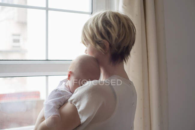 Mãe carregando bebê dormindo menina, olhando para fora da janela — Fotografia de Stock