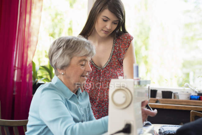 Neta assistindo avó usando máquina de costura — Fotografia de Stock