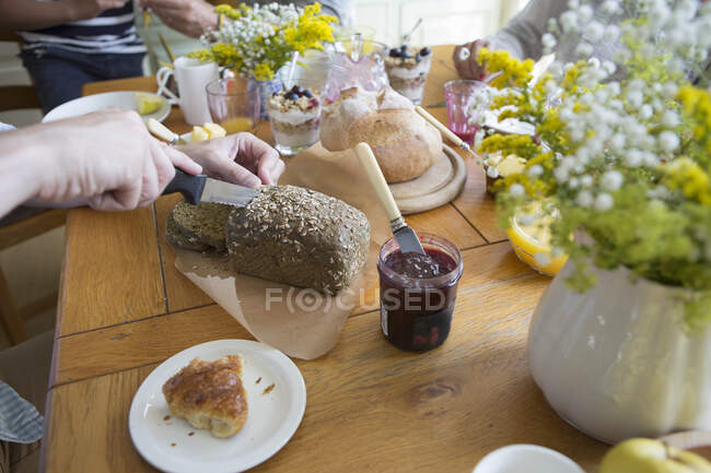 Hombre rebanando pan de granero en preparación para el desayuno, enfoque con las manos - foto de stock