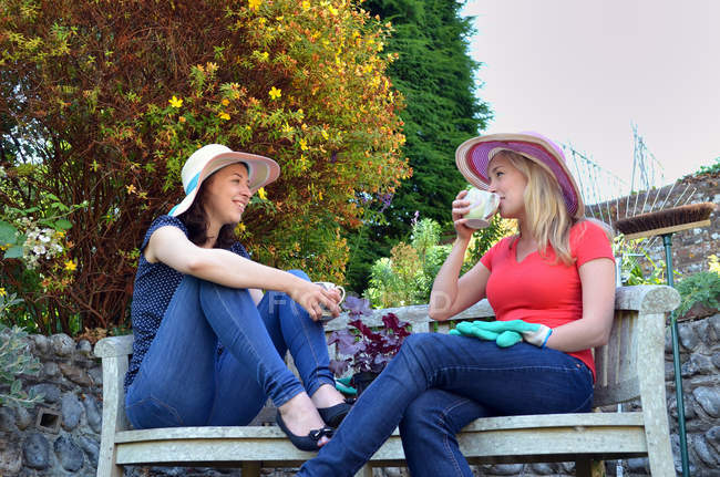 Porträt junger Frauen, die auf Bank sitzen und Tee trinken — Stockfoto