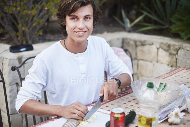 Junger Mann schneidet Brot am Terrassentisch — Stockfoto