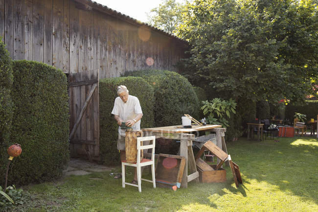 Старший чоловік робить дерев'яний ящик в саду — стокове фото