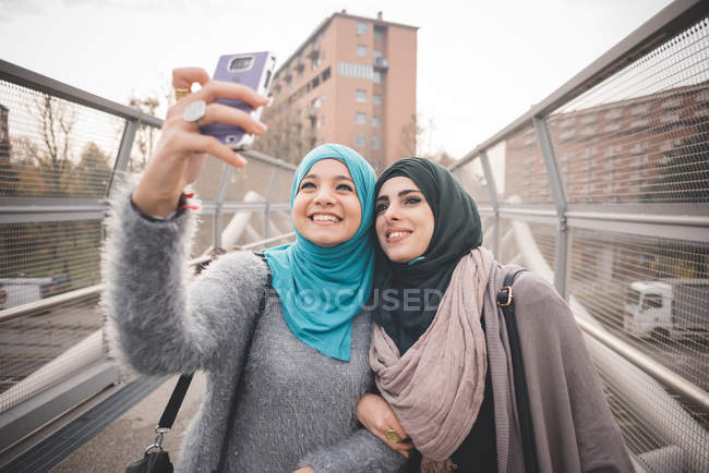 Две подруги на пешеходном мосту делают селфи на смартфоне — стоковое фото
