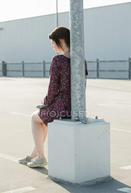 Jovem sentada encostada ao poste da lâmpada no estacionamento vazio — Fotografia de Stock