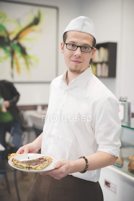 Young waiter serving food in cafe interior — Stock Photo