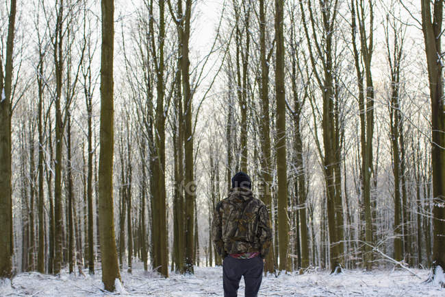 Visão traseira do jovem em pé na floresta coberta de neve com árvores nuas — Fotografia de Stock