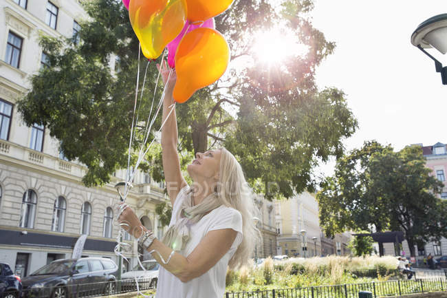 Mature woman, outdoors, holding bunch of balloons — Stock Photo