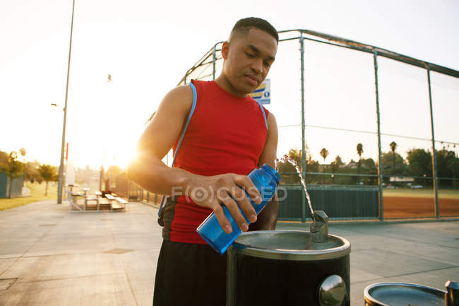 Young man filling water bottle from drinks fountain — Stock Photo