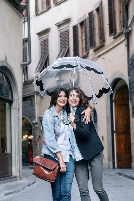 Coppia lesbica in piedi insieme in strada tenendo l'ombrello guardando la telecamera sorridente, Firenze, Toscana, Italia — Foto stock