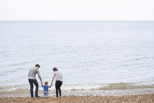 Jeune famille marchant sur la plage de galets, vue arrière — Photo de stock