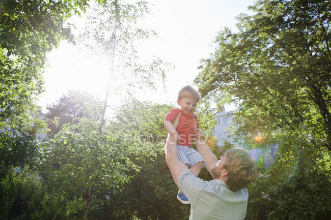 Father holding up toddler son in sunny park — Stock Photo
