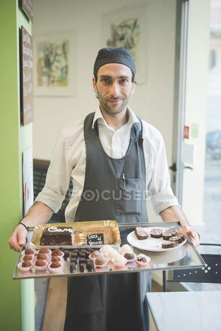 Waiter carrying tray of cakes and cookies in cafe — Stock Photo