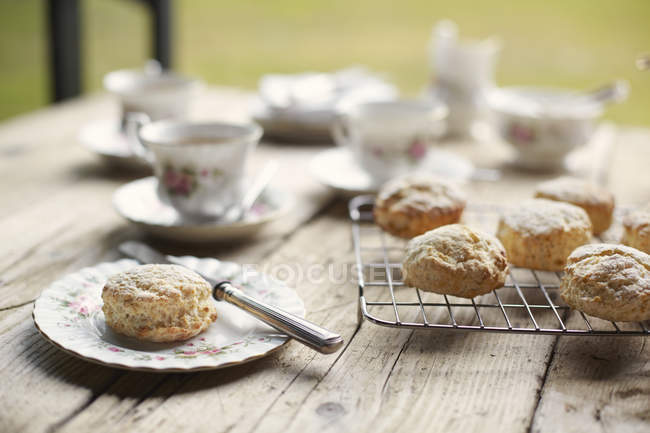 Table with fresh baked scones on cooling rack and plate — Stock Photo