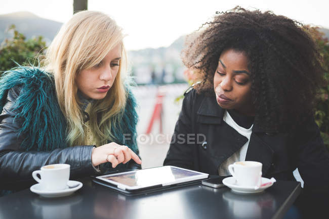 Дві молоді жінки використовують цифровий планшет у тротуарному кафе — стокове фото