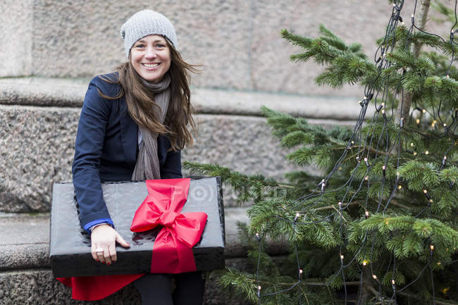 Retrato de mujer madura con regalo de Navidad al lado del árbol de Navidad - foto de stock