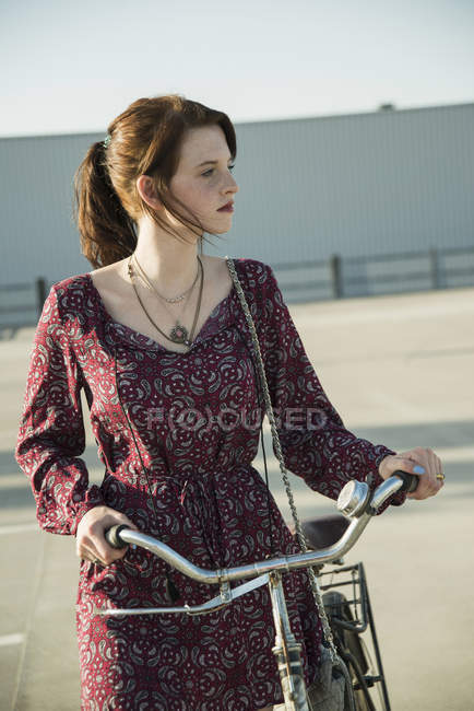 Young woman pushing bicycle in empty parking lot — Stock Photo