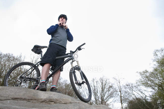 Älterer männlicher Mountainbiker befestigt Helm an Felsformation — Stockfoto