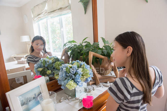Chica mirando en el espejo y jugueteando con su pelo - foto de stock