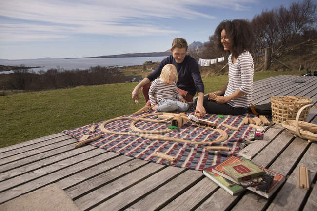 Мальчик и родители играют с игрушечным поездом на деревянной палубе — стоковое фото
