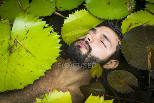 Высокоугольный вид бородатого молодого человека, плавающего среди лиловых подушечек с закрытыми глазами, Тайба, Сеара, Бразилия — стоковое фото