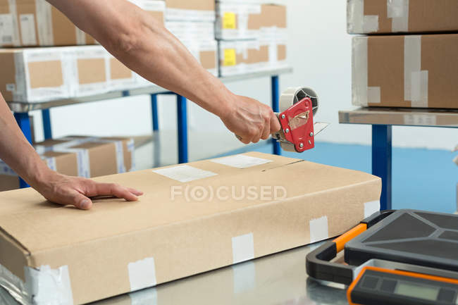 Hands of warehouse worker taping parcel in distribution warehouse — Stock Photo