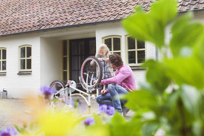 Padre e hija reparando bicicleta en frente de la casa de campo - foto de stock