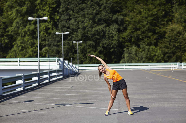 Young female runner stretching in parking lot — Stock Photo