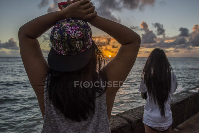 Две молодые женщины, наблюдающие за восходом солнца, пляж Каава, Оаху, Гавайи, США — стоковое фото