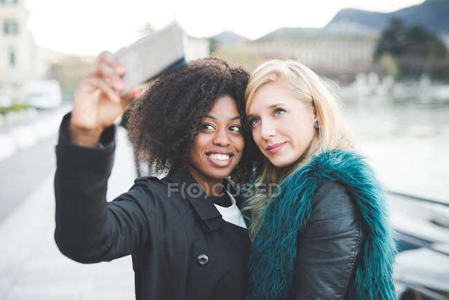 Duas jovens posando para selfie ao lado do lago — Fotografia de Stock