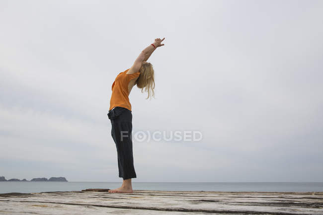 Mitte erwachsene Frau streckt sich zurück und praktiziert Yoga auf einem hölzernen Seebrücke — Stockfoto