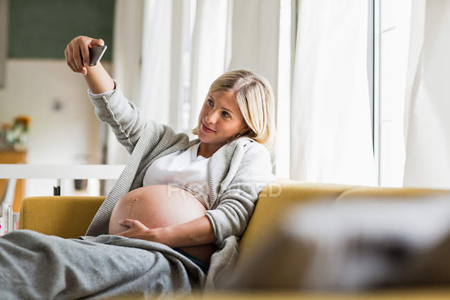 Повна вагітність молода жінка на дивані приймає селфі — стокове фото