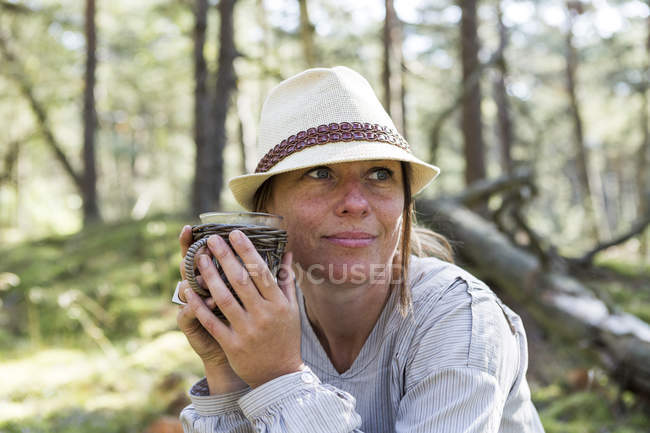 Reife Frau trägt Fedora, trinkt Tee im Wald — Stockfoto