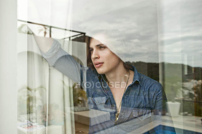 Jeune homme regardant par la fenêtre de l'hôtel — Photo de stock