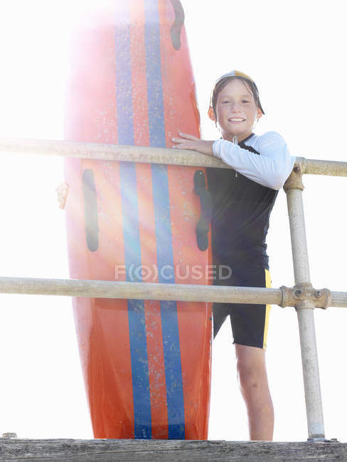 Portrait of boy nipper (child surf life savers) leaning against railings in sunlight, Altona, Melbourne, Australia — Stock Photo