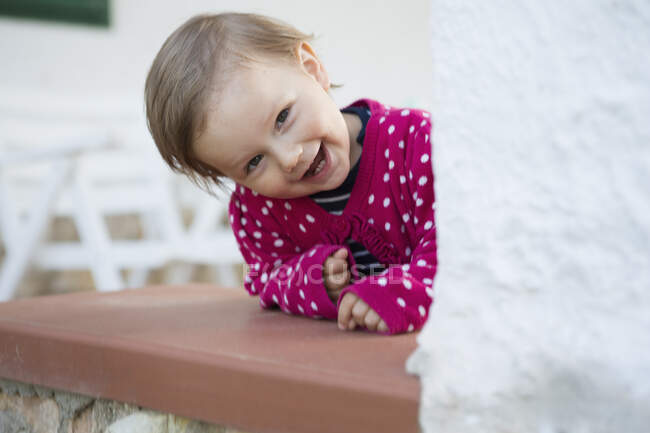Portrait of female toddler leaning forward and peeking from table — Stock Photo