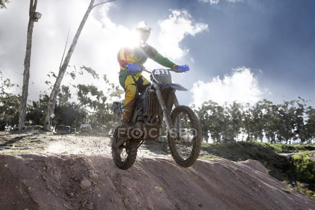 Young male motocross racer jumping mid air down mud hill — Stock Photo