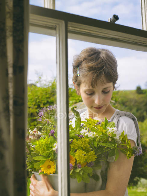 Jeune femme dehors fenêtre avec un bol de fleurs sauvages — Photo de stock