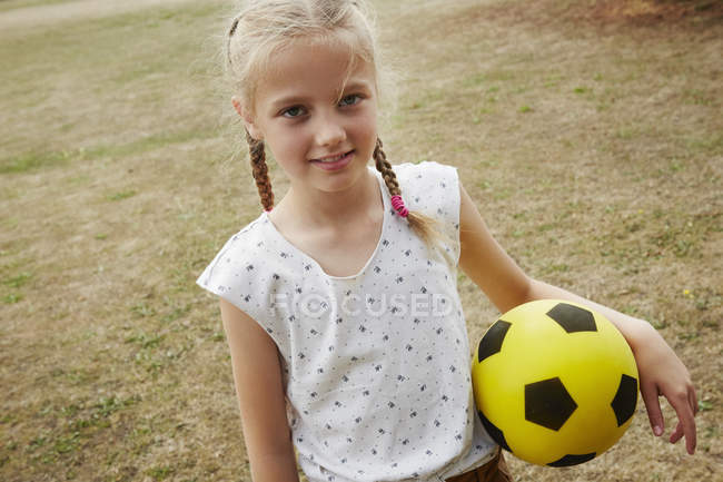 Hochwinkelaufnahme von Mädchen mit Zöpfen, die Fußball halten und in die Kamera schauen — Stockfoto