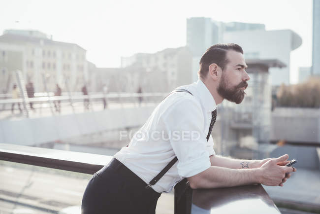 Стильный бизнесмен со смартфоном, выглядывающий с балкона офиса — стоковое фото