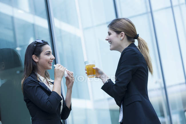 Businesswomen having lunch with sandwich and drink by office building — Stock Photo